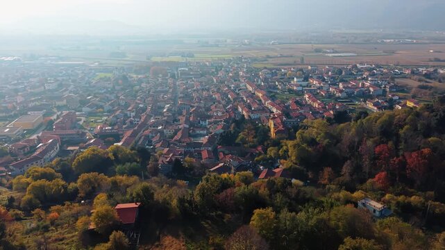 Aerial view of Montalto Dora reveals a tapestry of terracotta roofs nestled amidst autumnal trees, creating a warm contrast against the distant landscape, Montalto Dora, Piedmont, italy.