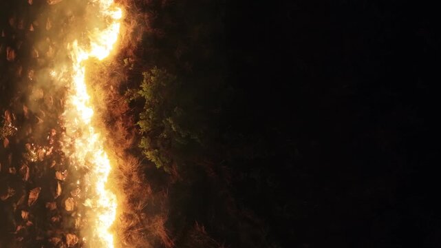 Aerial view of a wildfire's fierce, bright flames juxtapose against the dark, scorched earth in a stark, dramatic landscape, Thabazimbi, Waterberg District Municipality, South Africa.