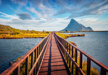 Fototapeta premium Wonderful summer scenery. Picturesque summer view of Spiaggia di Porto Taverna beach with wooden footpath bridge. Marvelous morning scene of Sardinia island, Italy. Beauty of nature concept background
