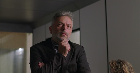 Obraz premium Close up of mature businessman with hand on chin and focused expression while considering decision during corporate meeting in modern office