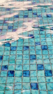 Calming abstract footage of blue swimming pool tiles with gentle water movement and soft reflections, creating a relaxing background texture suitable for wellness, spa, summer, and travel themes.
