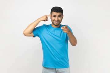 Displeased attractive unshaven man showing stupid gesture, pointing at camera with frowning face.