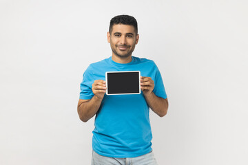 Optimistic satisfied man standing showing tablet with black bank screen, advertisement area.