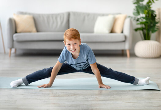 A sporty ginger boy performs a leg-split on a fitness mat in his living room. This adorable preteen is stretching and training his body in a cozy home setting perfect for exercise.