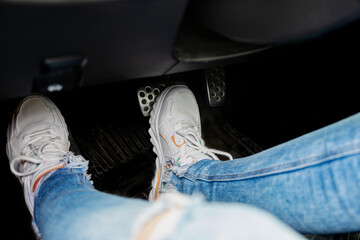 Feet in white sneakerson car brake pedal close-up