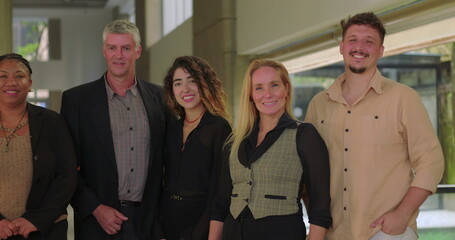 Close up of smiling diverse office team standing together, happy business professionals in bright corporate hallway, friendly group portrait with natural expression