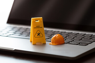 Toy hard hat, "Under Construction" sign with crossed tools on a laptop, symbolizing system maintenance, repair, and upgrades