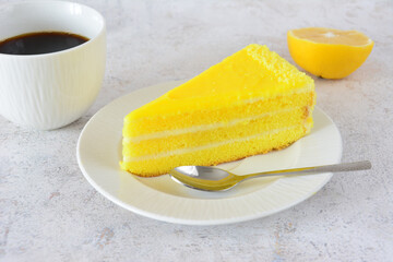 a white cup of coffee with a slice of layered lemon cake on saucer