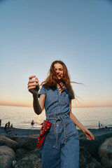 lifestyle woman in modern boho-western denim street style enjoying sunset by the sea with film...