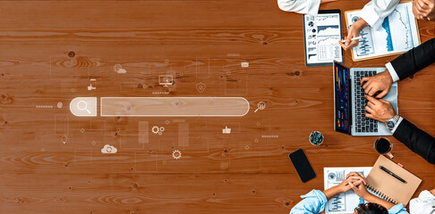 Aerial view of a business team engaged in digital marketing strategy session with laptop, charts, and a search bar concept on a wooden desk. Trope