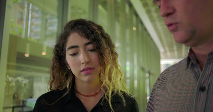 Close up of young woman looking at tablet with thoughtful expression, standing next to male colleague during discussion, focused on content in office environment