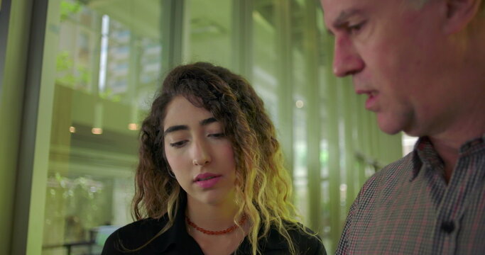 Close up of young woman looking at tablet with thoughtful expression, standing next to male colleague during discussion, focused on content in office environment