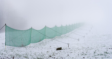 Grüne Schutznetze gegen Schneewehen an der Landstraße und Feld bei Nebel und Reif