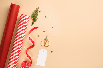 Christmas gift wrapping with red and white striped wrapping paper, ribbon, scissors, thuja spruce on beige backdrop. Copy space.