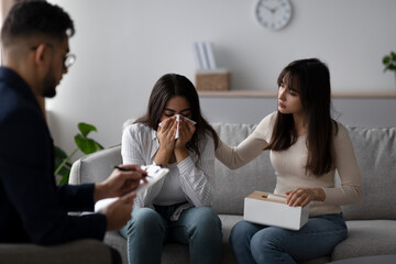 In a counseling session, a young middle eastern woman cries while her partner comforts her. They seek guidance from a psychologist to address their relationship challenges.