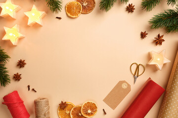 Christmas frame with star candles, dried oranges, spices, and wrapping paper on beige background. Copy space for text or design.