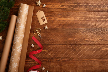 Christmas wrapping paper rolls, ribbon, and scissors on dark wooden background. Rustic festive flat...