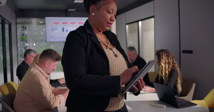Close-up of African American businesswoman using digital tablet during meeting, team collaborating in background in modern conference room
