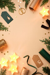 Christmas frame with star candles, fir branches, gift tags, and wrapping supplies on beige background. Copy space for text or design.