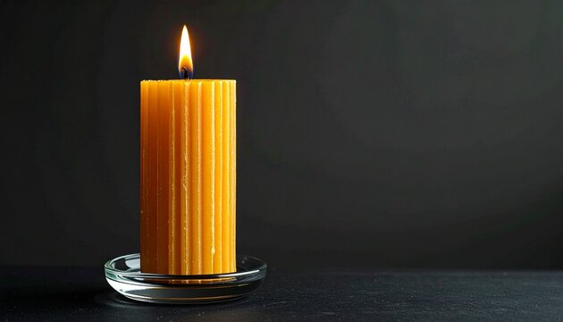 Vertically ribbed yellow candle in clear glass holder on black background