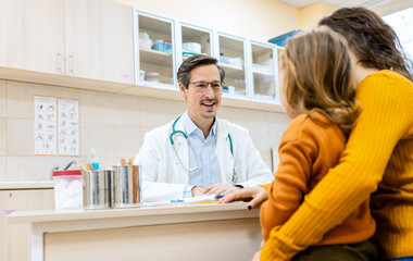 Fototapeta premium Male pediatrician consulting with a woman and her young child during a medical checkup in clinic.