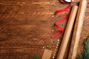 Christmas wrapping background with paper rolls, ribbon, and scissors on dark wooden desk. Copy space for text.