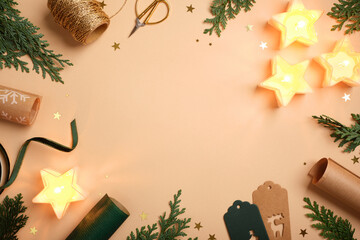 Christmas frame with star candles, fir branches, gift tags, and wrapping supplies on beige background. Copy space for text or design.