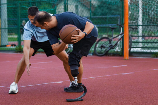 A man with a prosthetic leg skillfully dribbles a basketball on an outdoor court, showing determination and strength. - Powered by Adobe