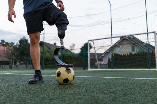 A man with a prosthetic leg skillfully plays soccer on a grassy field during the evening.