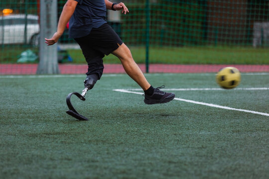 A man using a prosthetic leg skillfully plays soccer during a game on a grassy field in the late afternoon.