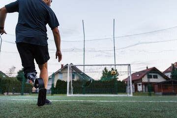 A man with a prosthetic leg runs towards a soccer goal, actively engaged in the sport on a grassy field at dusk.