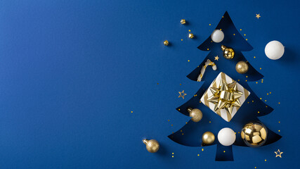 A festive Christmas tree silhouette on a blue backdrop decorated with a gold gift box, baubles, and...
