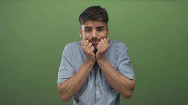 Man wearing pale blue shirt clenching fists with visible forearms in studio under green lighting; anxiety doubt.