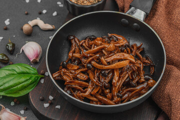 Fried Shimeji mushrooms with garlic, basil, and spices in a pan, served on a dark background