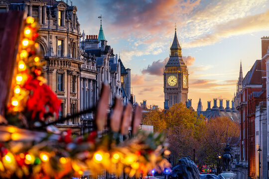 Winter sunset view of the Big Ben clock tower in London, England, with blurred fairy lights from the Trafalgar Square Christmas market in front