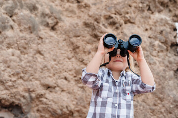 Portrait of playful child using binoculars outdoors. Little girl watching binoculars. Concept of childhood, adventure, imagination and discovery.