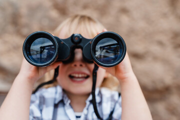 Obraz premium Portrait of playful child using binoculars outdoors. Little girl watching binoculars. Concept of childhood, adventure, imagination and discovery.