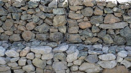 Close-up of a stone gabion wall construction with gray and brown rocks held by wire mesh, engineering concept, background