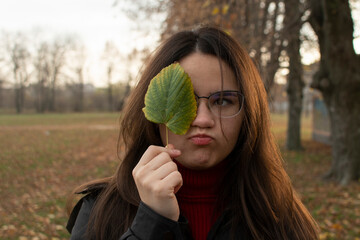 Portrait of a young attractive woman in eyeglasses covering her face with a leaf	