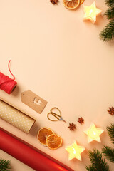 Christmas gift wrapping with star candles, dried oranges, spices, and wrapping paper on beige background. Place for text or design.