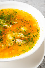 A close-up vertical studio shot from above of a white bowl filled with golden chicken and potato soup garnished with fresh green dill on a gray marble background