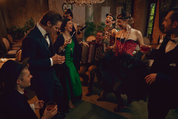 Retro group laughing and dancing with accordion player during lively vintage party night. Concept...