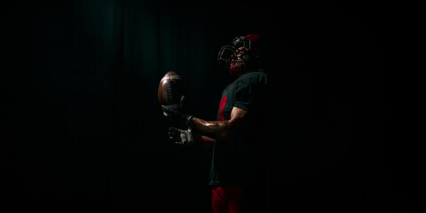 American football player lifting ball with proud emotional energy in dramatic light. Concept of motivational posters, branding, sport hero content, training inspiration.