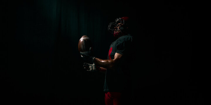 American football player lifting ball with proud emotional energy in dramatic light. Concept of motivational posters, branding, sport hero content, training inspiration.