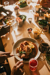 A group of people are sitting at a table with plates of food and drinks. Scene is casual and social, as the people are enjoying a meal together