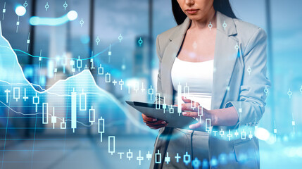 Woman in business attire using a tablet, with transparent candlestick charts overlaid, in a modern office setting, representing finance and investment concept