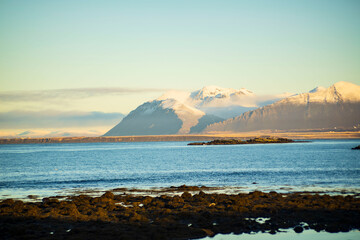 Snow-Covered Mountains and Rocky Shoreline in Soft Morning Light