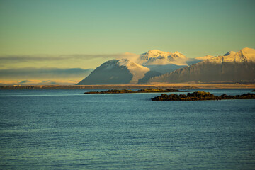 Snowy Mountain Range Above Calm Sea and Rocky Islets at Sunrise