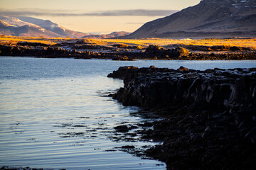 Rocky Coastline with Calm Water and Sunlit Distant Hills in Winter