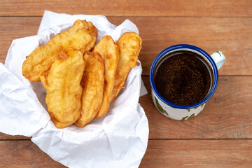 Overhead view of golden fried bananas (Pisang Goreng) served with black coffee in a traditional enamel mug on a rustic wooden table. Asian snack/dessert.